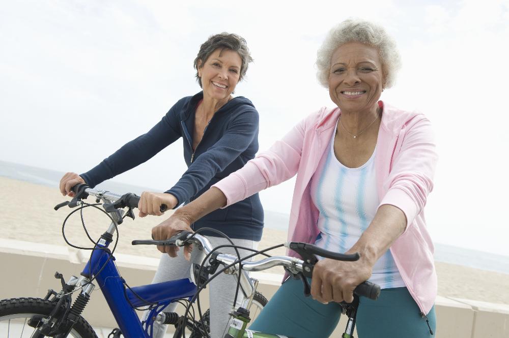 two middle-aged women riding their bikes near the ocean