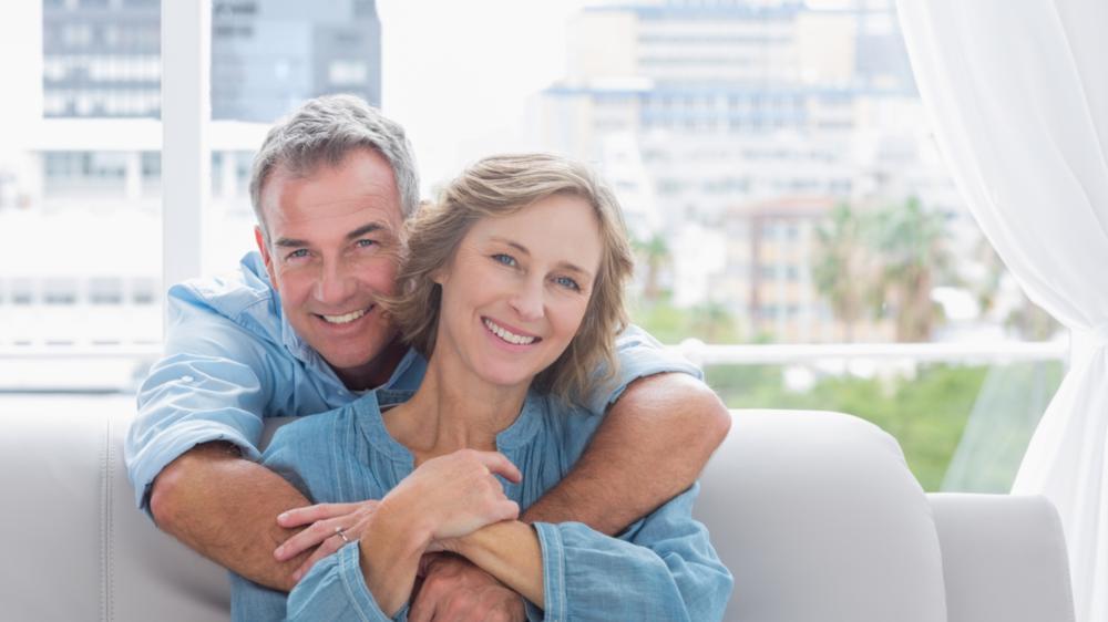 man hugging woman from behind while she sits on the couch in anderson