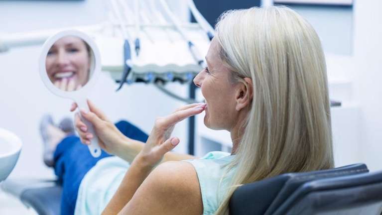 woman smiling at dental mirror after cosmetic dentistry in anderson, SC